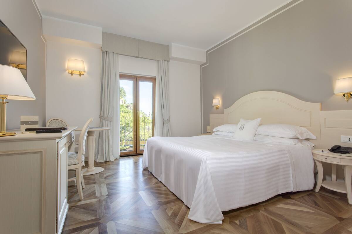 Une chambre d’hôtel avec un grand lit, un bureau avec une lampe, une chaise et une vue sur l’extérieur.