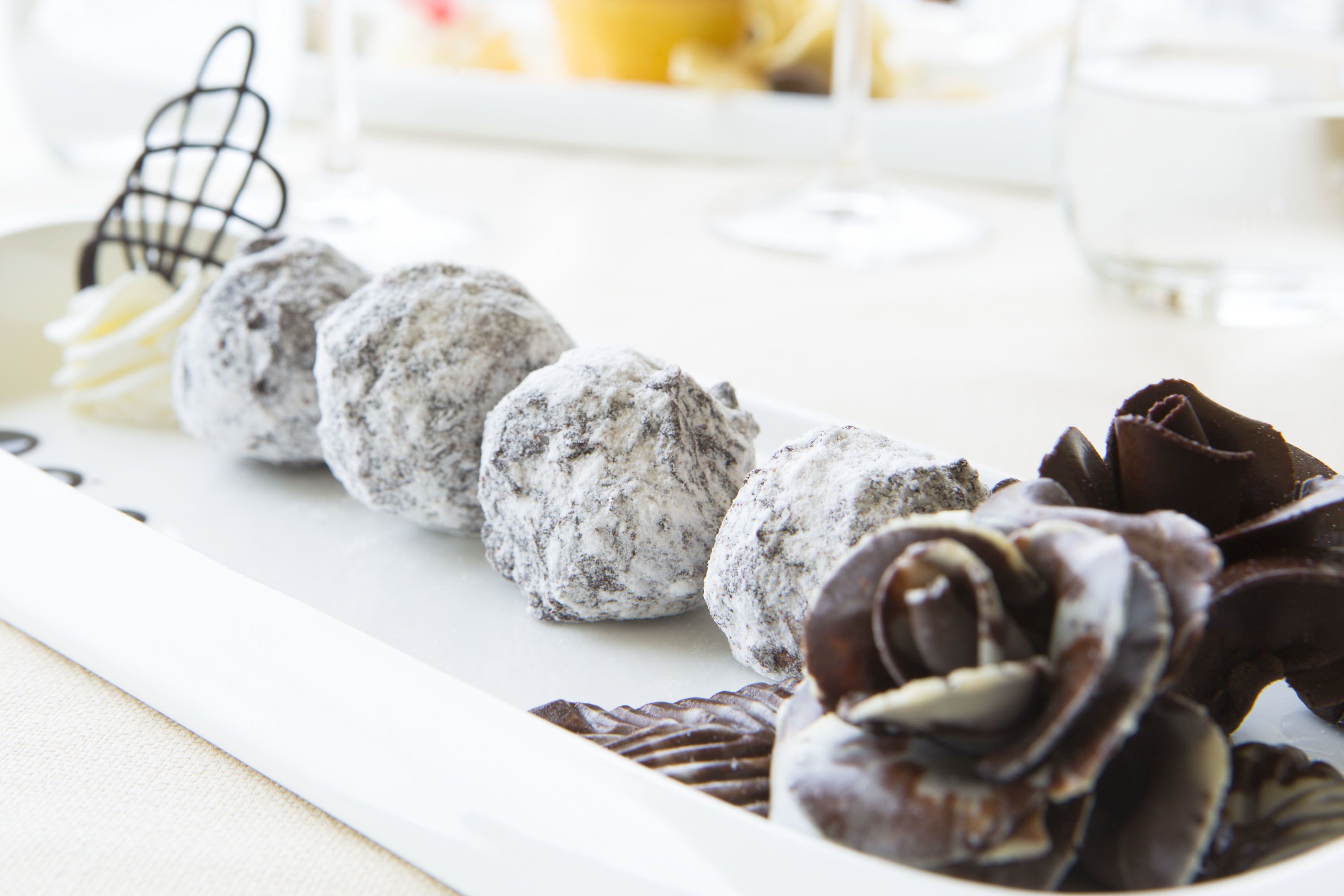 A dessert tray with various sweets, including chocolate roses and powdered sugar-covered balls, on a white plate.
