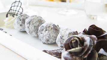 A dessert tray with various sweets, including chocolate roses and powdered sugar-covered balls, on a white plate.