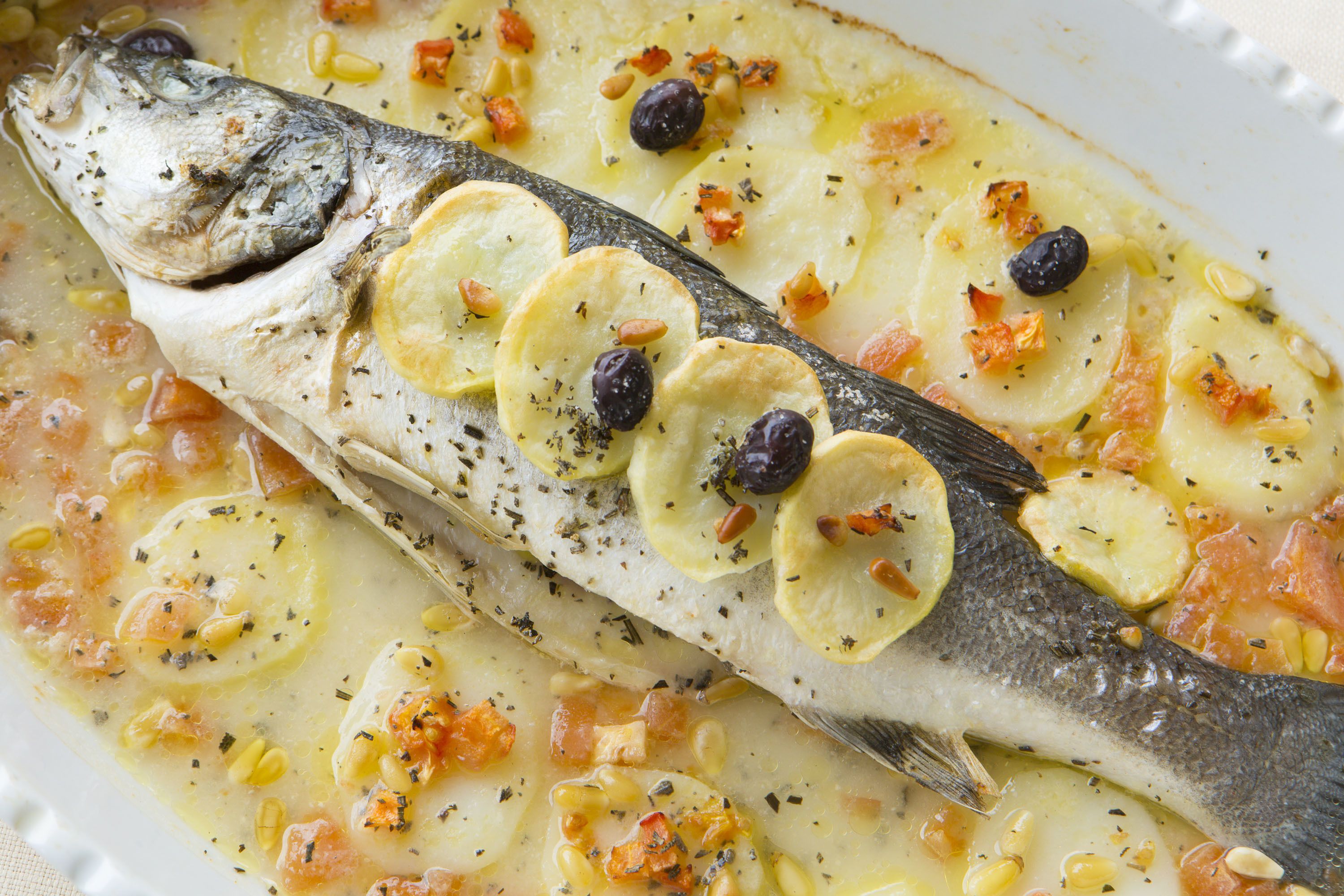A fish with sliced potatoes and olives on top.