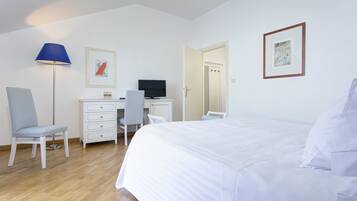 A hotel room with a bed, a desk with a computer, a chair, a lamp, and artwork on the walls.