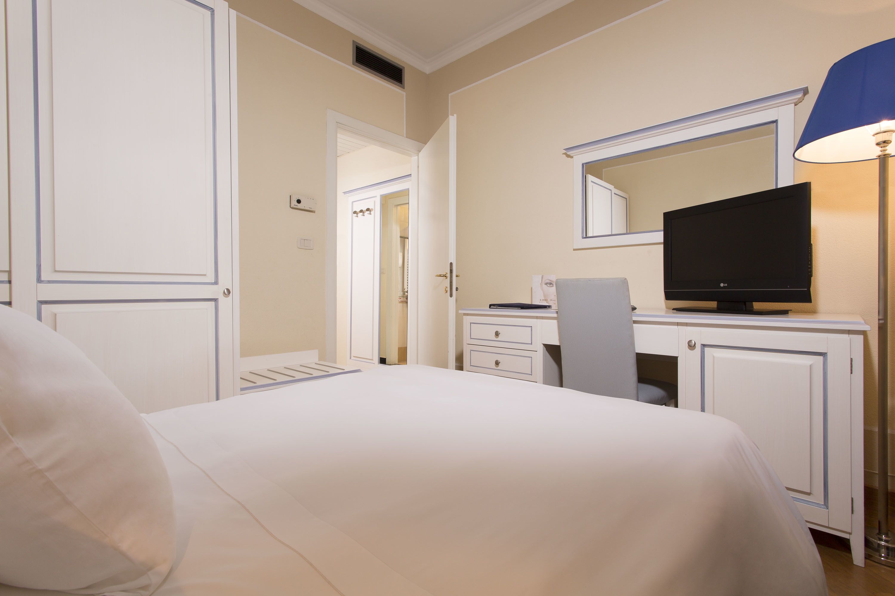 A hotel room with a bed, a desk with a television, a lamp, and a wardrobe.