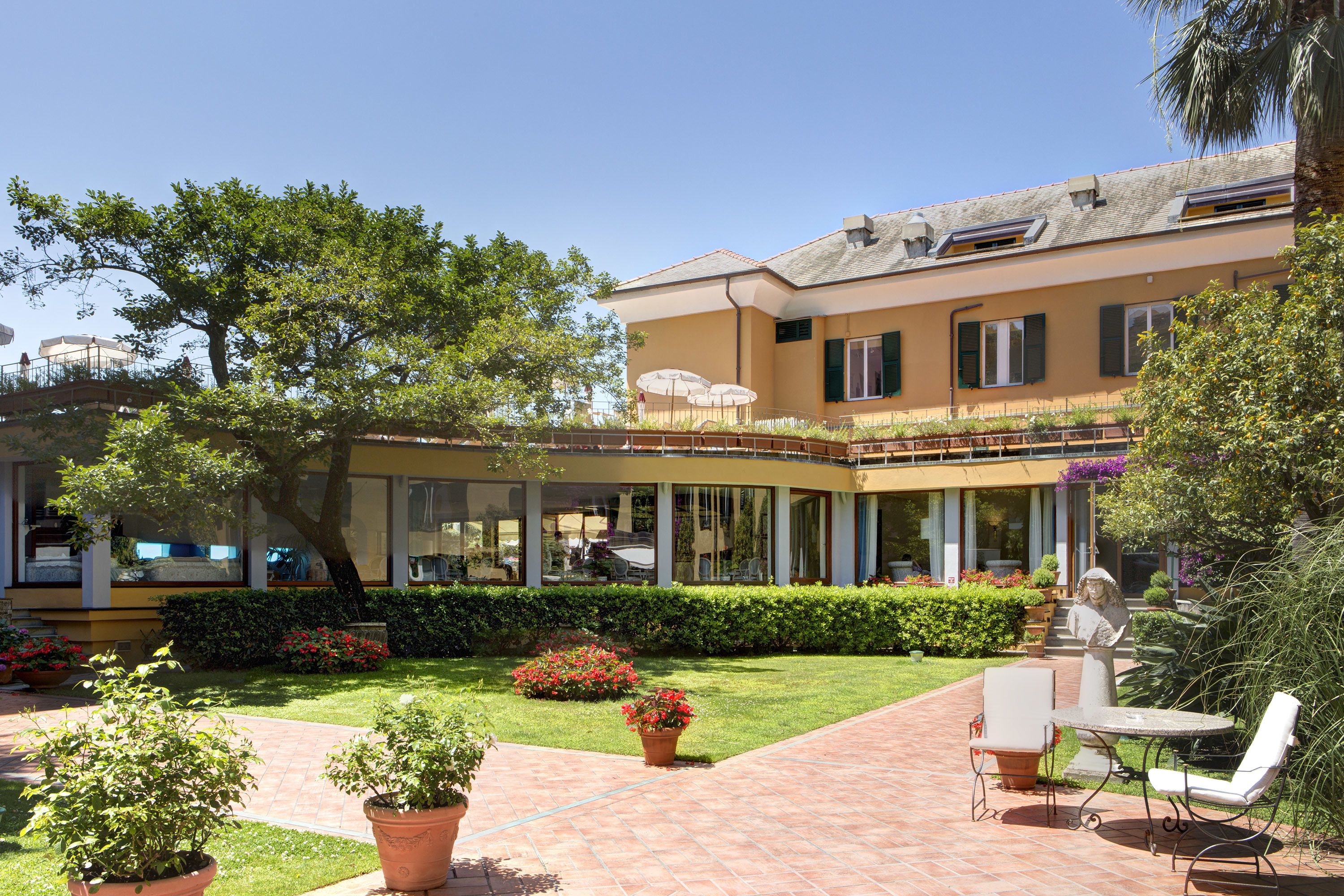 Un patio con un edificio, plantas en macetas y mobiliario exterior.