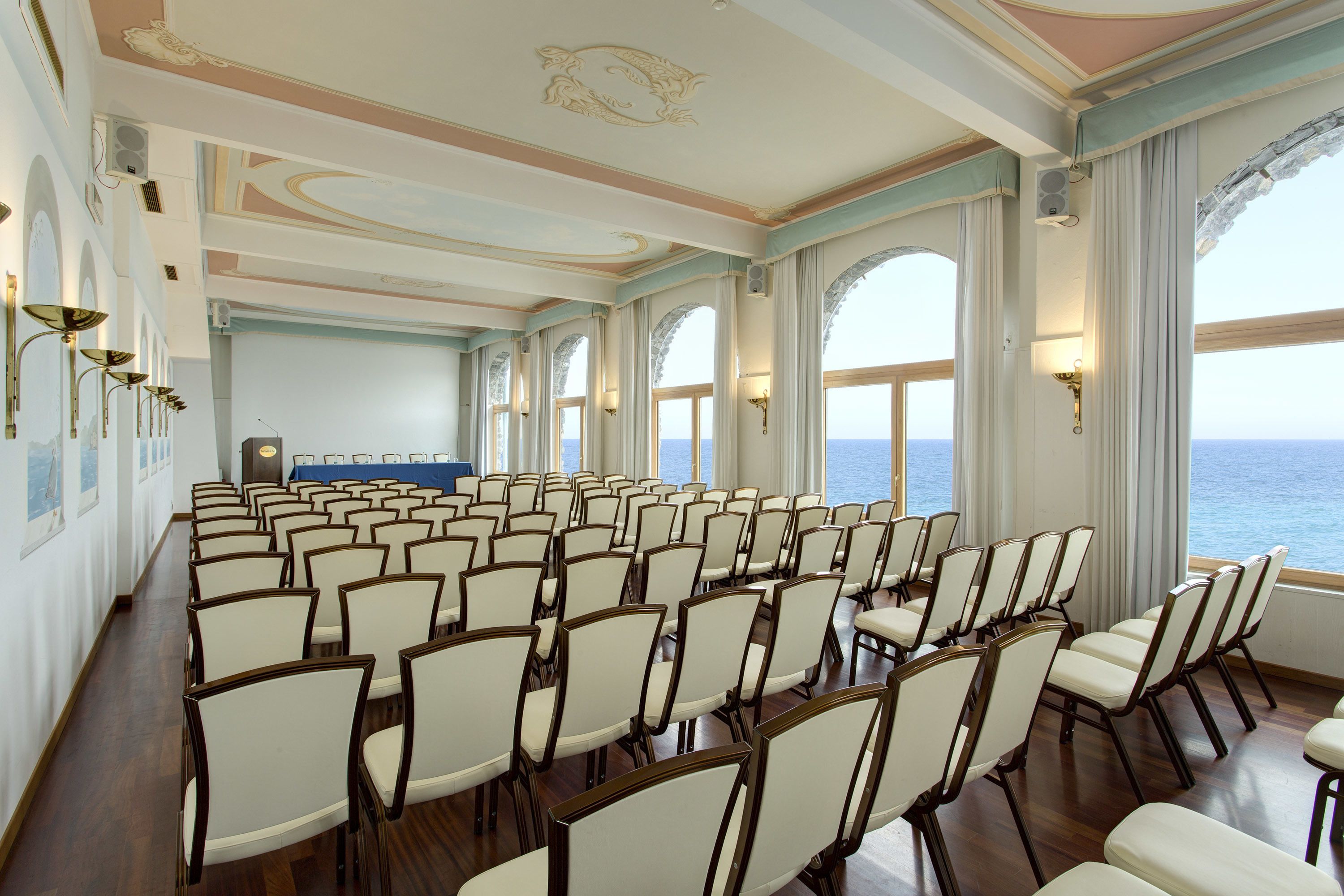 Une salle de conférence avec des rangées de chaises, de grandes fenêtres et une vue sur la mer.