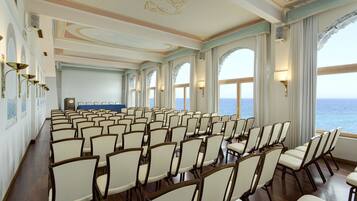 Une salle de conférence avec des rangées de chaises, de grandes fenêtres et une vue sur la mer.