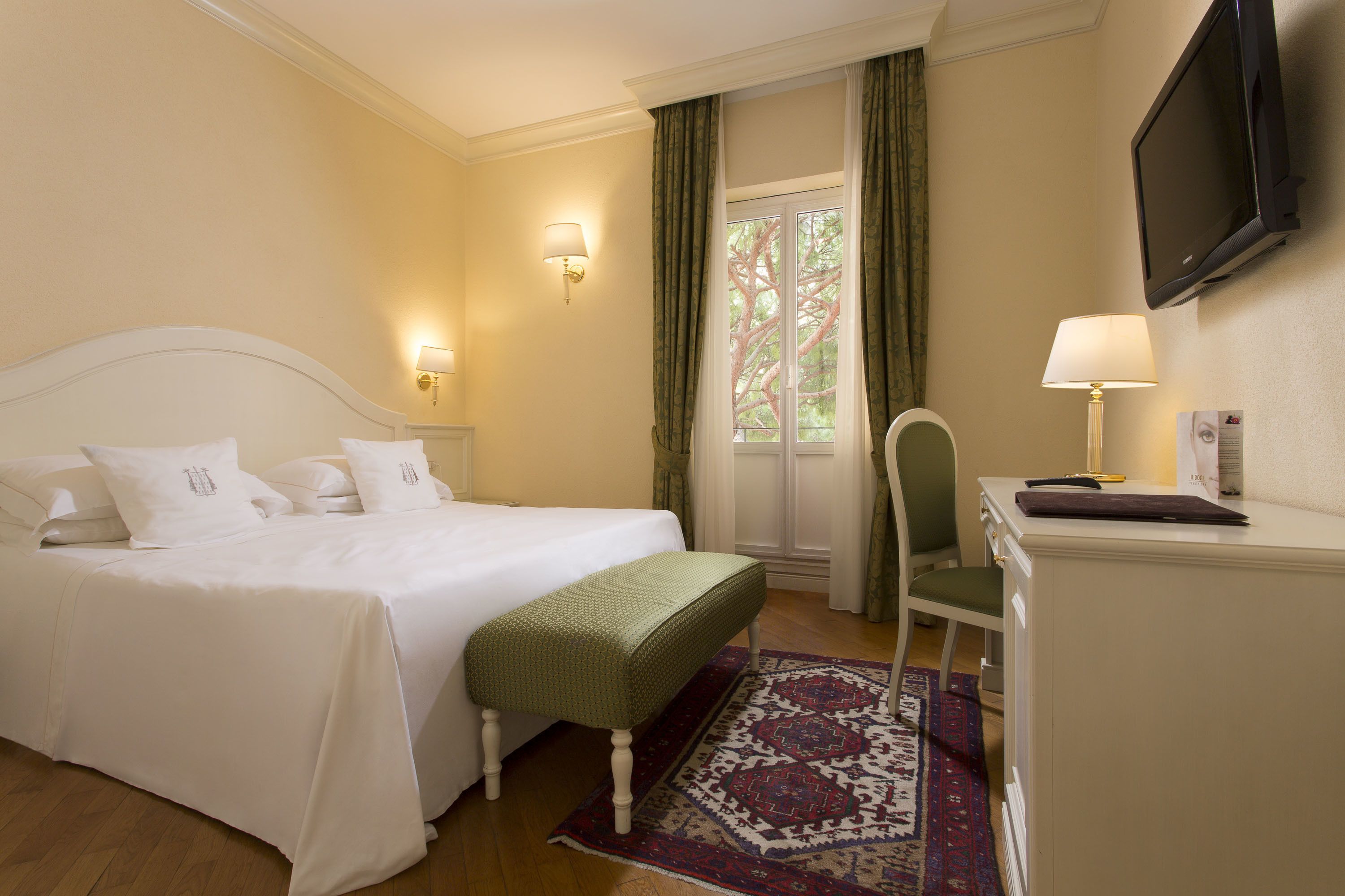 A hotel room with a bed, a desk, a chair, a TV, and a window with curtains.