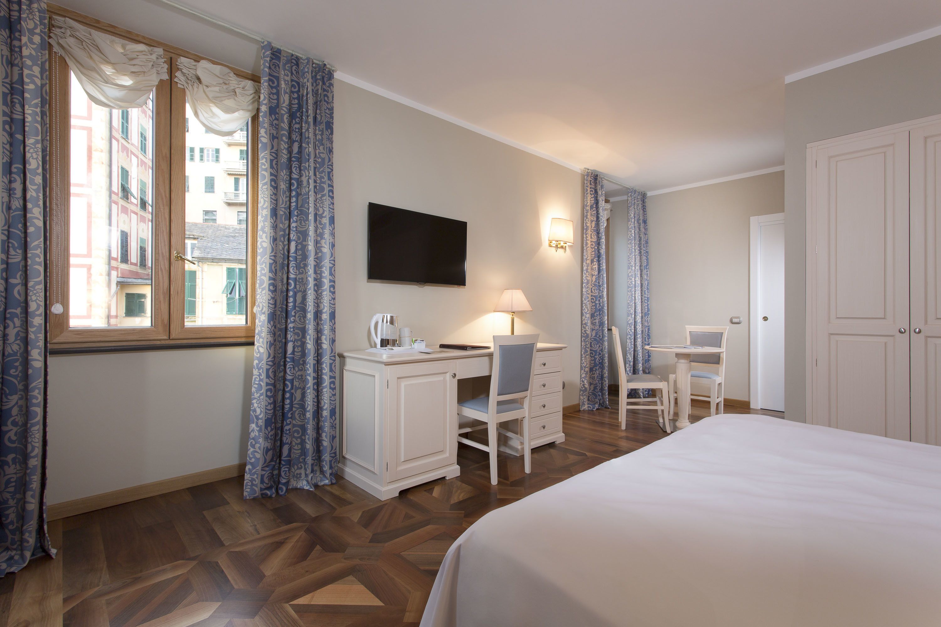 A hotel room with a bed, a desk with a chair, a TV, and a window with curtains.