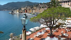 A seaside terrace with outdoor seating and a view of the sea and buildings. - Hotel Cenobio Dei Dogi (Camogli)
