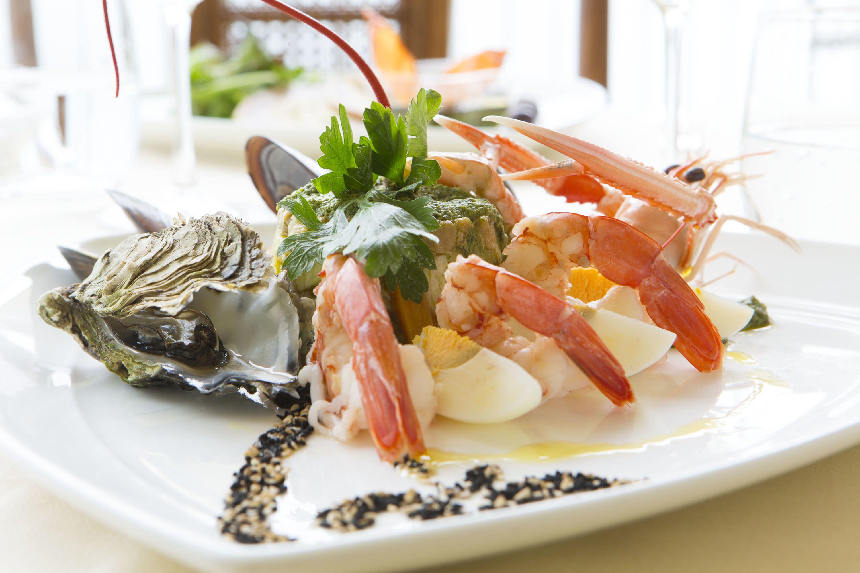 Un plat de fruits de mer composé de crevettes, d’huîtres et de légumes verts, servi dans une assiette blanche.