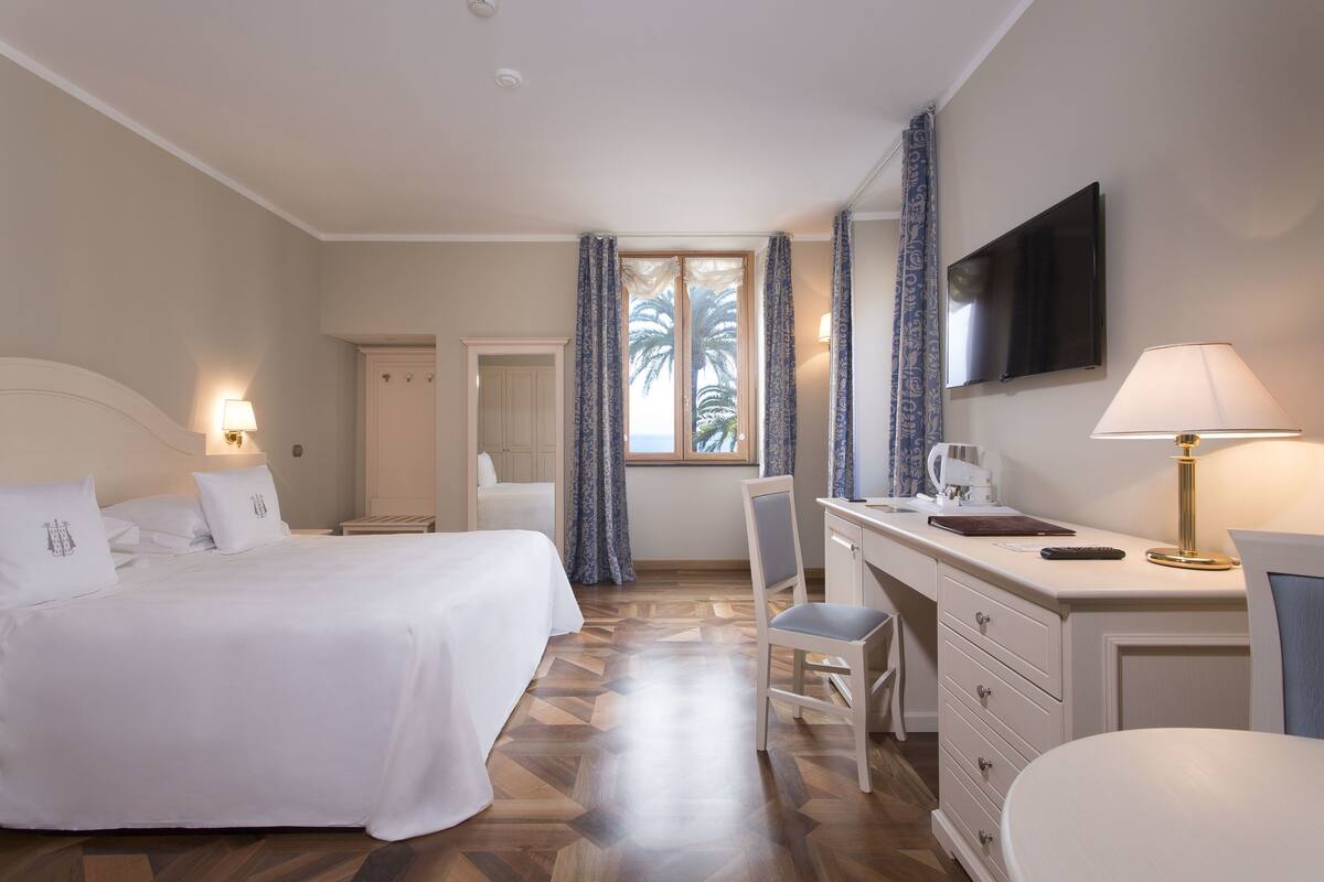 Une chambre d’hôtel équipée d’un lit, d’un bureau, d’une chaise, d’une télévision et d’une fenêtre avec des rideaux.