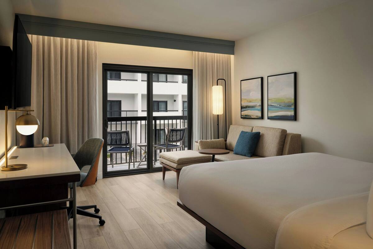 Hotelkamer met een bed, bureau, stoel en een balkon met uitzicht op het gebouw.