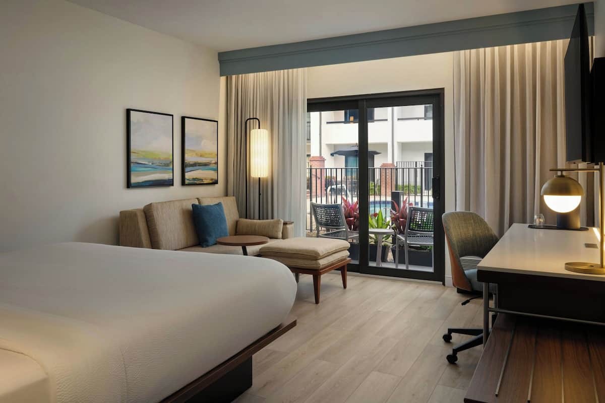 Een hotelkamer met een groot bed, een bureau, een stoel, een bank en een balkon met uitzicht.