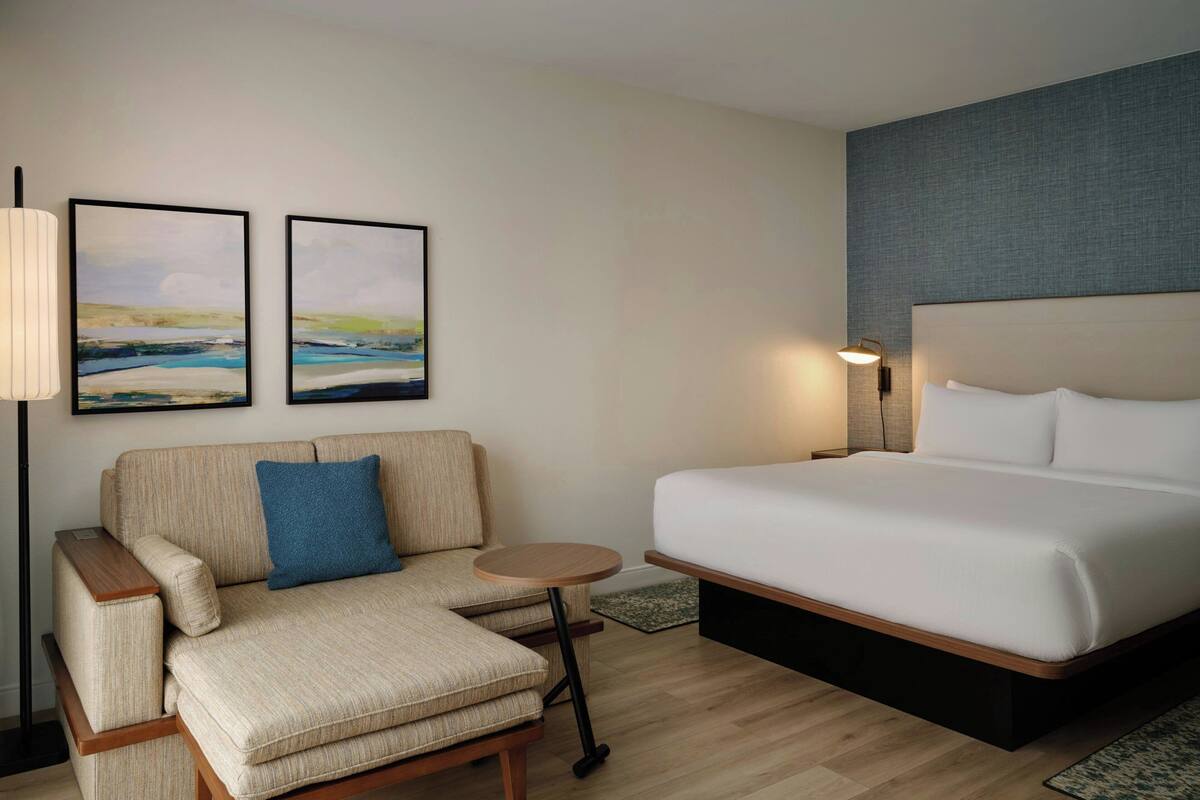 Una habitación de hotel con una cama, un sofá, una mesita redonda y dos cuadros en la pared.