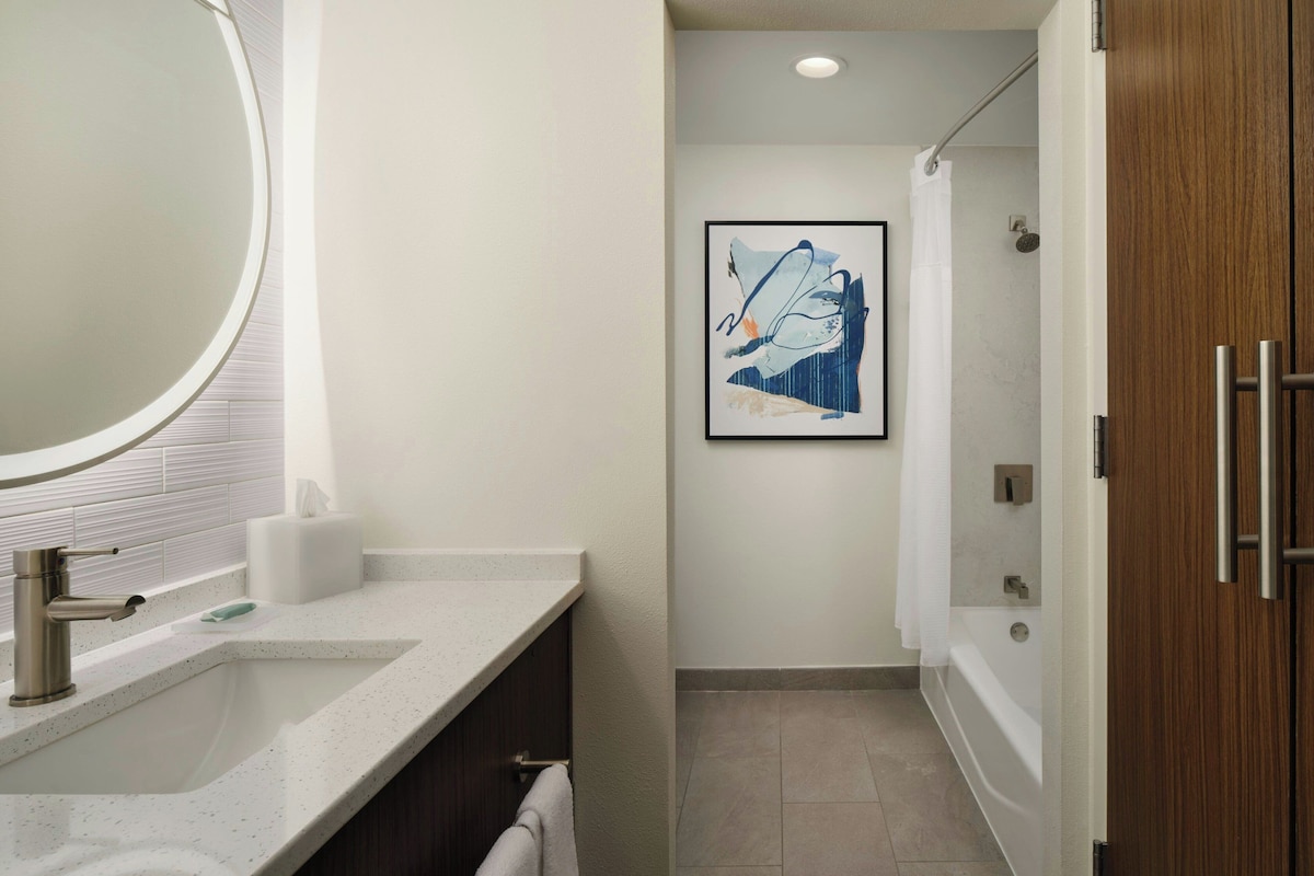 Een moderne badkamer met een grote spiegel, een wastafel, een douche en een kunstwerk in een lijst aan de muur.