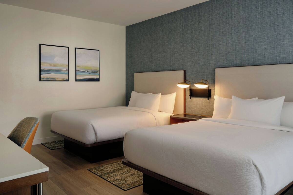 Habitación de hotel con dos camas, un escritorio y dos lámparas de pared.