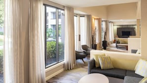 A modern hotel room with a large window, a sofa, a coffee table, and a TV in the living area. - Courtyard by Marriott Orlando Airport (Orlando)