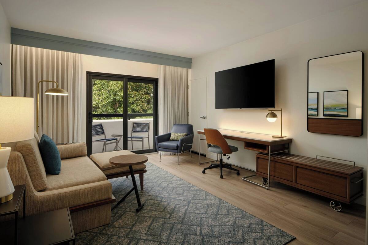Hotelkamer met een bank, bureau, stoel, televisie en uitzicht door het raam.
