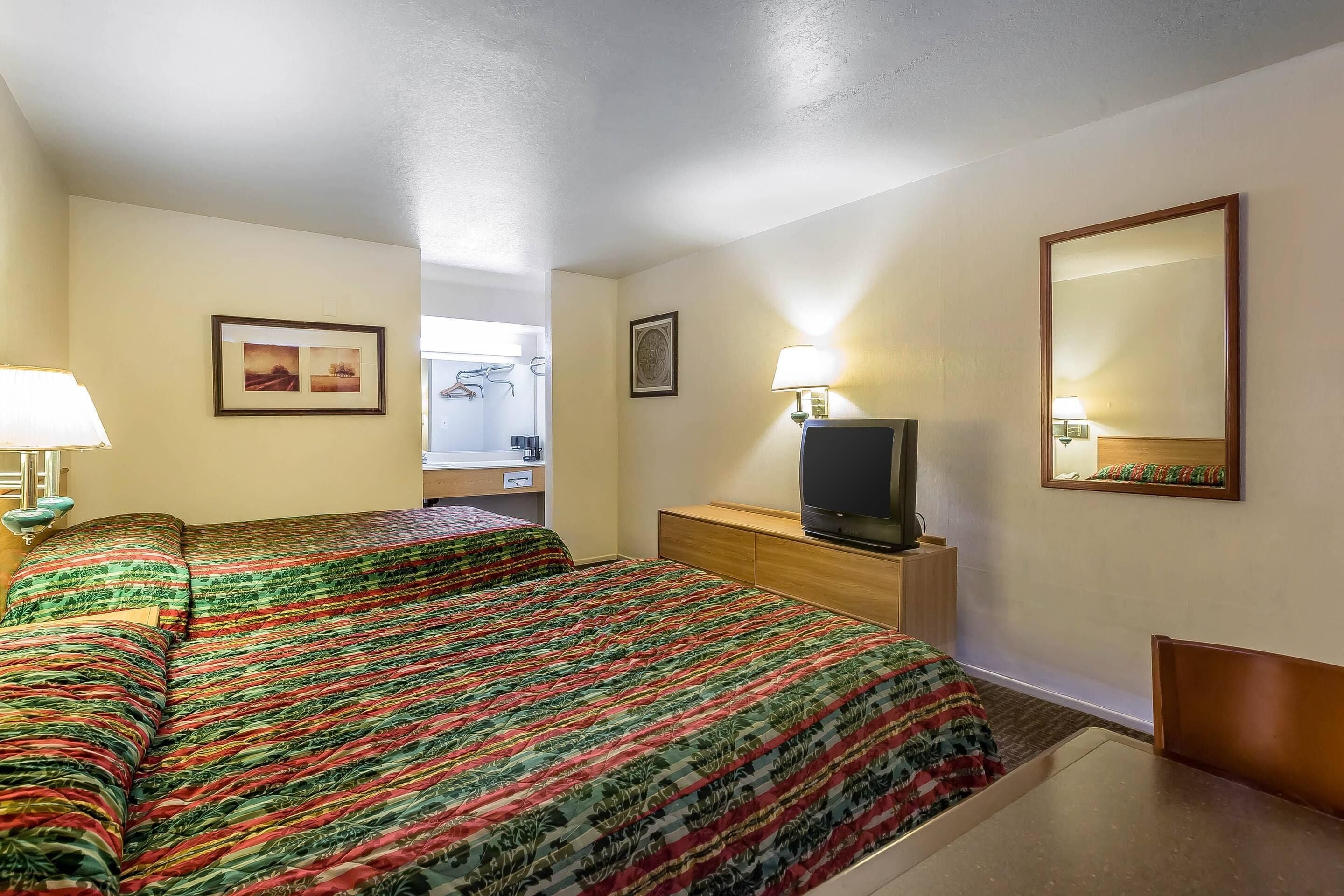 Une chambre d’hôtel avec deux lits, une télévision, un bureau et un miroir.