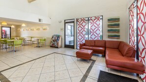 A lobby with a brown leather sofa, green and white chairs, a magazine rack, and patterned walls. - Rodeway Inn Magic Mountain Area (Castaic)