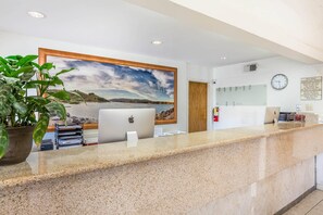 A hotel reception desk with a computer, a large landscape painting, a clock, and a fire extinguisher.