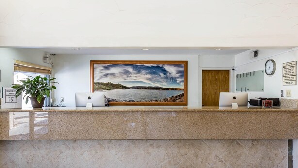 A reception desk with a painting of a landscape, a clock, and a potted plant. - Rodeway Inn Magic Mountain Area (Castaic)