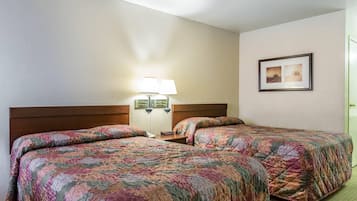 A hotel room with two beds, a nightstand, a lamp, and a framed picture on the wall.