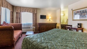 A hotel room with a large bed, a sofa, a desk with a lamp, a television, and a window with curtains. - Rodeway Inn Magic Mountain Area (Castaic)