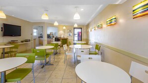 A modern dining area with round tables and green chairs, a kitchen in the background, and decorative wall art. - Rodeway Inn Magic Mountain Area (Castaic)