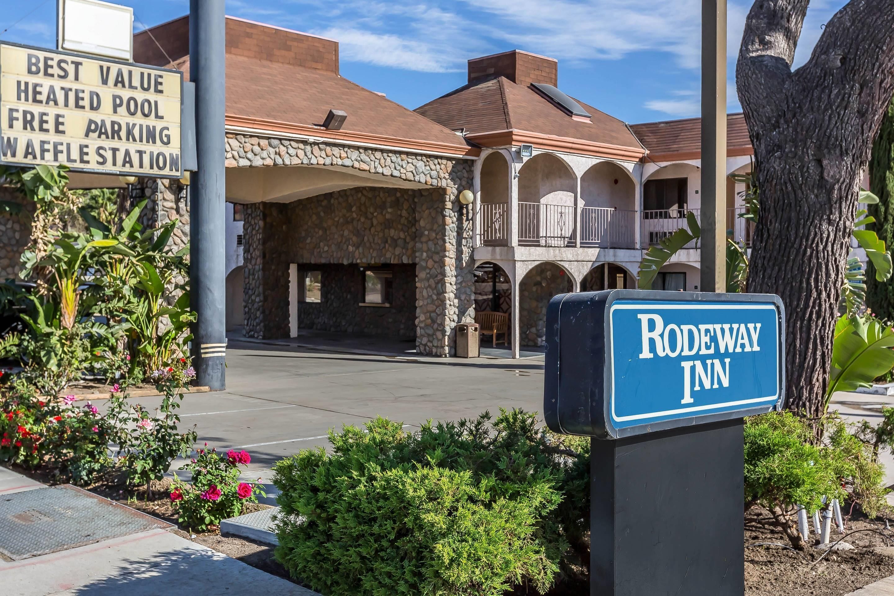 A hotel entrance with a sign for Rodeway Inn, a stone building with a covered patio, and a parking area with a sign offering best value amenities.