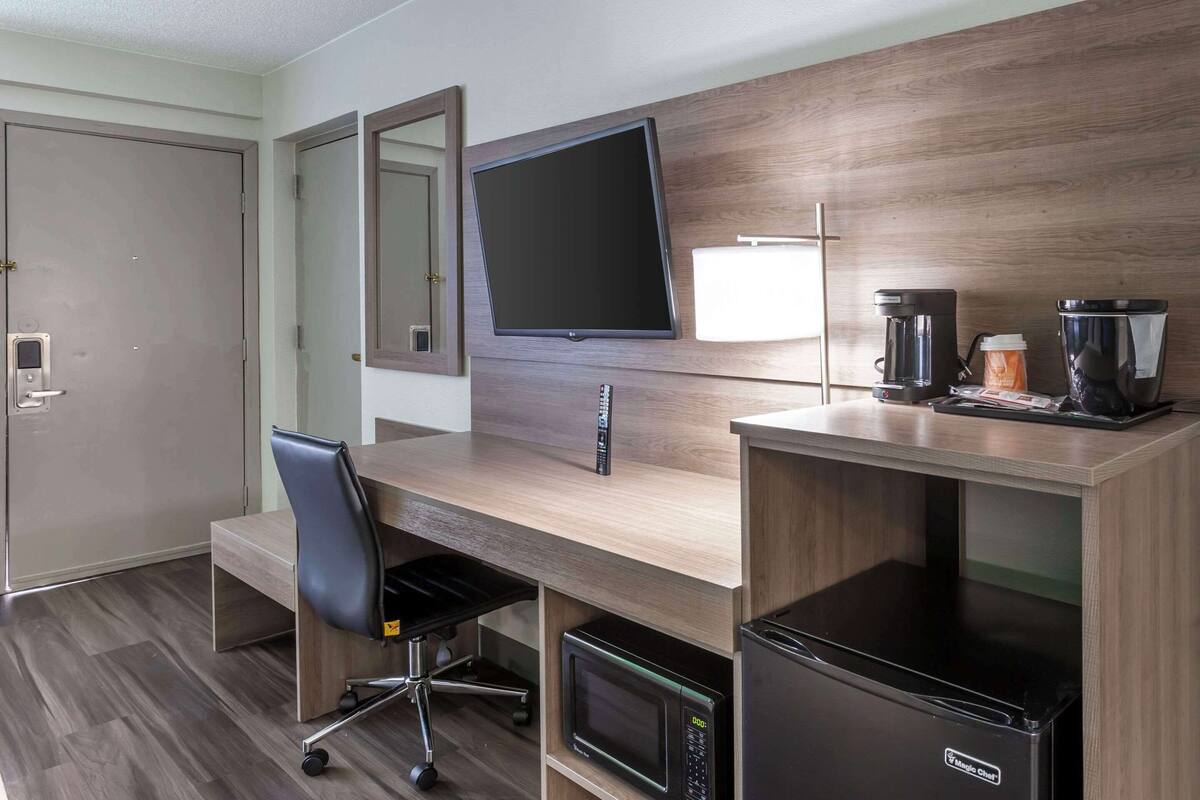 A hotel room with a wooden desk, a flat-screen TV, a coffee maker, a microwave, and a refrigerator.