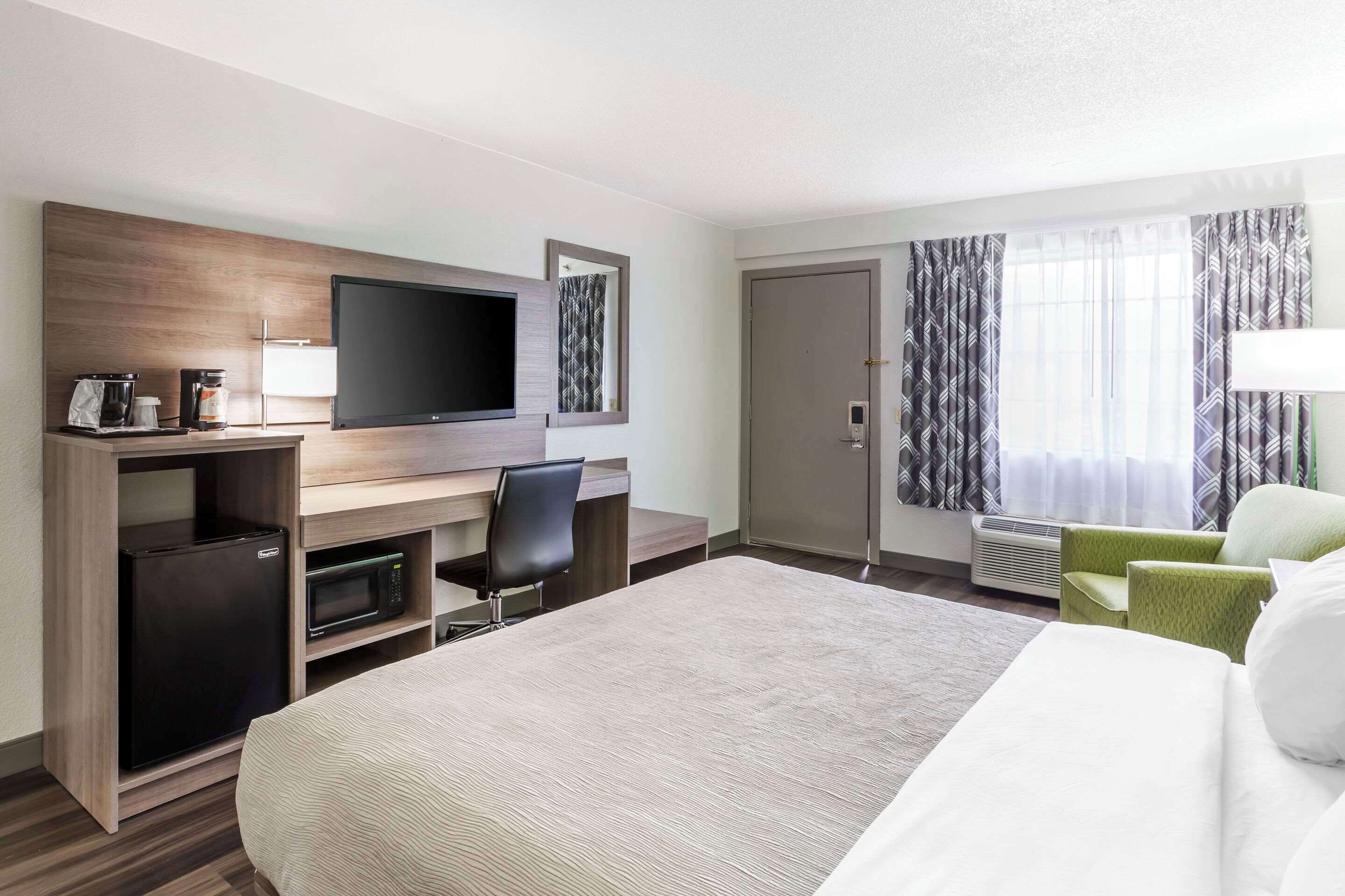 Habitación de hotel con cama, escritorio con televisor de pantalla plana, microondas, refrigerador pequeño y sillón verde.