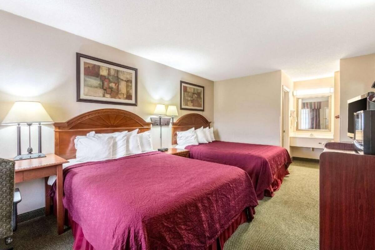 A hotel room with two beds, a desk, a chair, a TV, and artwork on the walls.