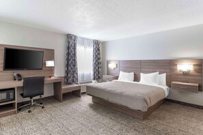 Habitación de hotel con cama, escritorio, televisor, lámpara y ventana con cortinas.