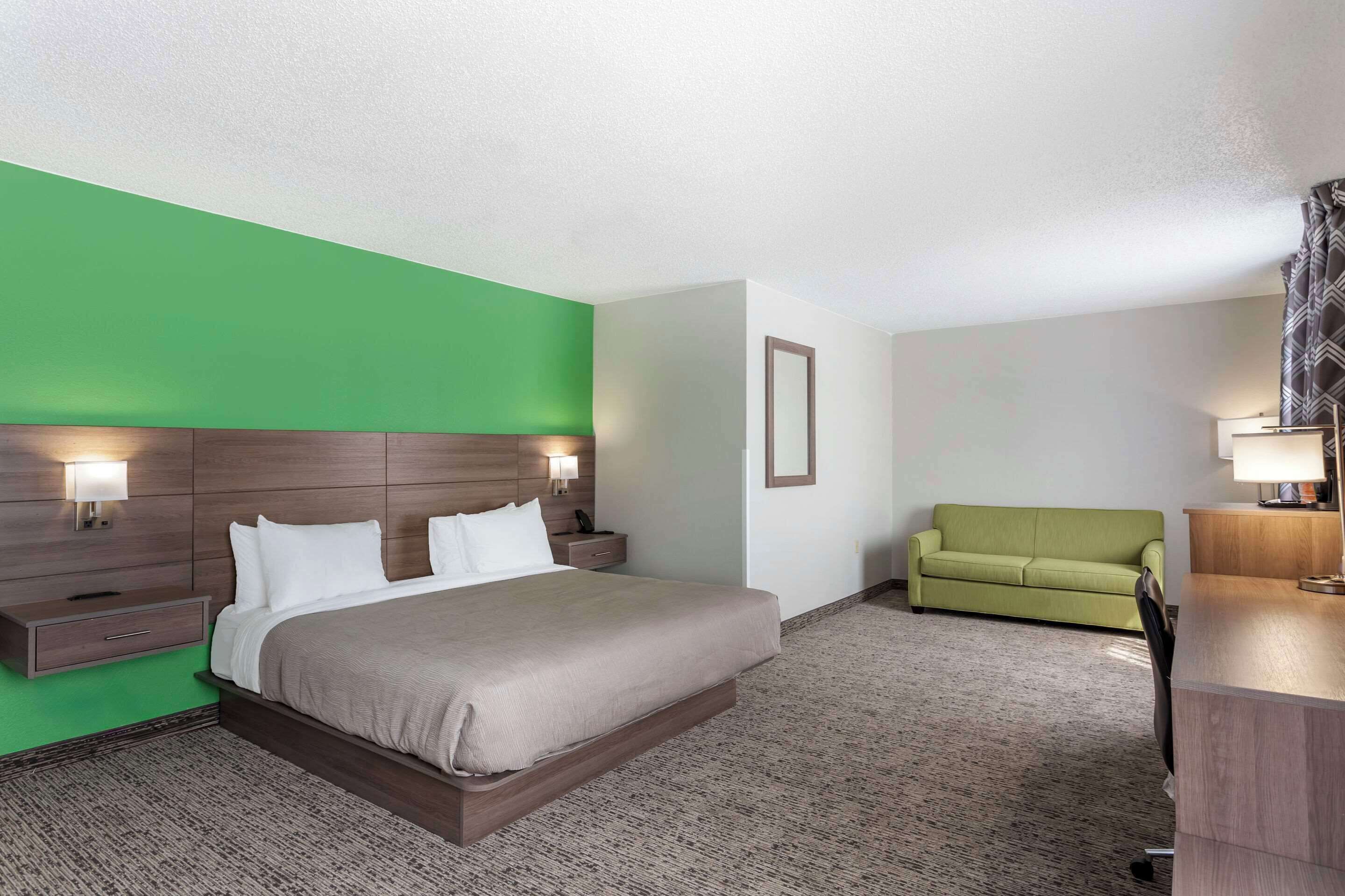 A hotel room with a bed, bedside tables, a green wall, a green sofa, and a desk with a lamp.
