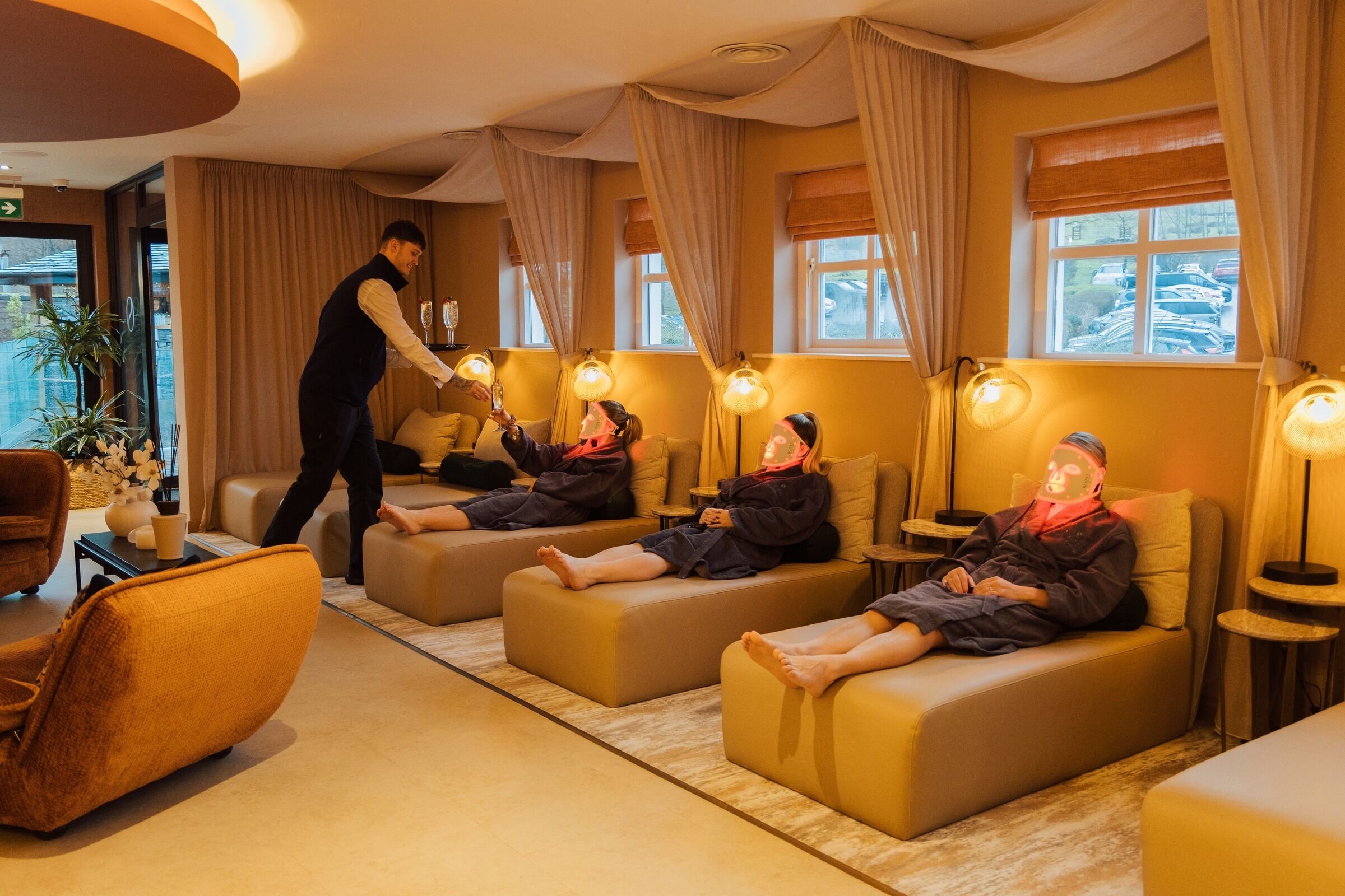 A hotel room with a massage area featuring three massage tables, a reception desk, and a large window with curtains.