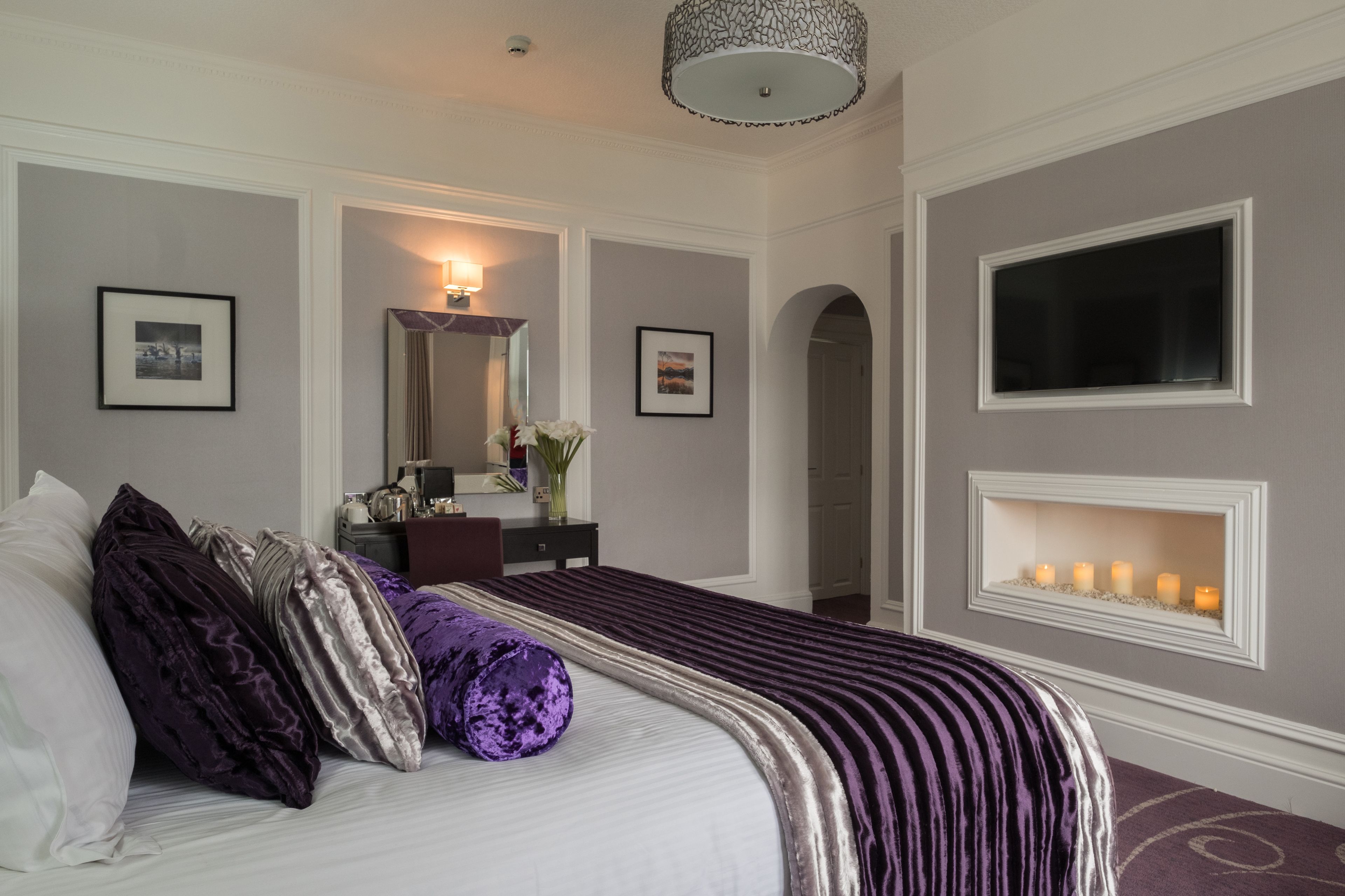A neatly arranged bedroom with a large bed, a dresser, a mirror, and a wall-mounted TV.