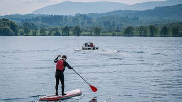 A person paddleboarding on a calm lake with a boat in the background and hills in the distance.