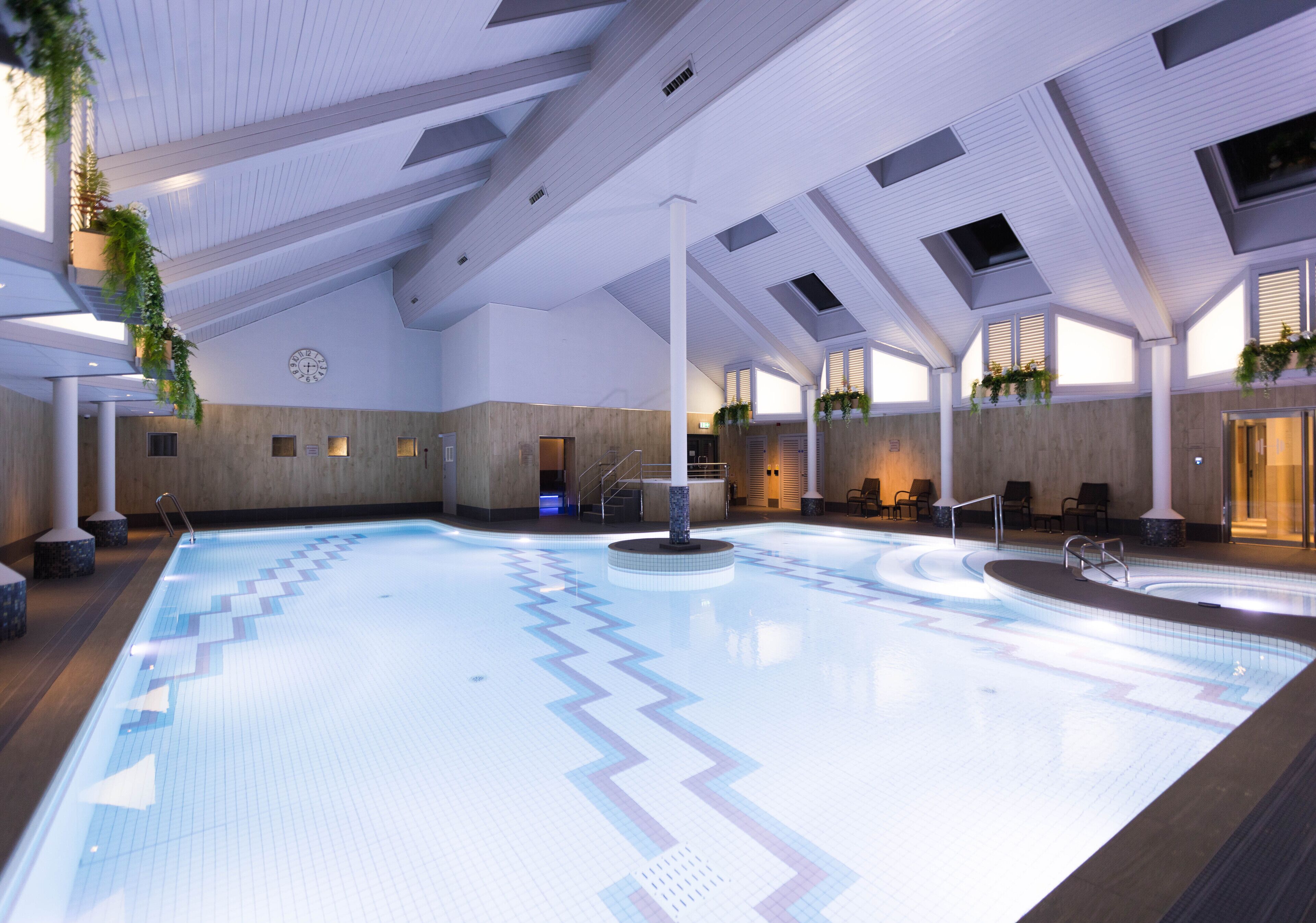 An indoor swimming pool with a geometric tile pattern, skylights, and potted plants.