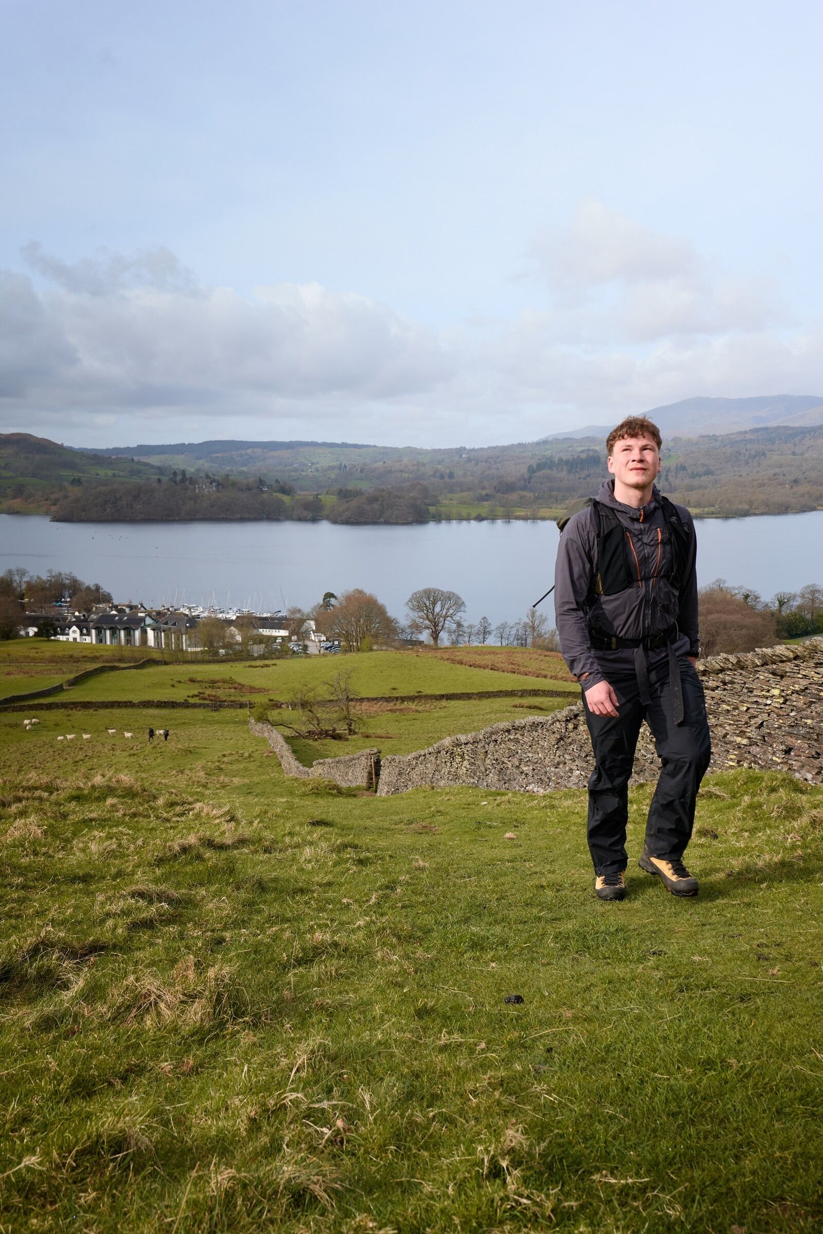 A person standing on a grassy hill overlooking a lake with houses in the background.