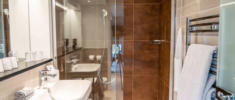 Un baño moderno con ducha de vidrio, lavamanos blanco y un perchero para toallas.