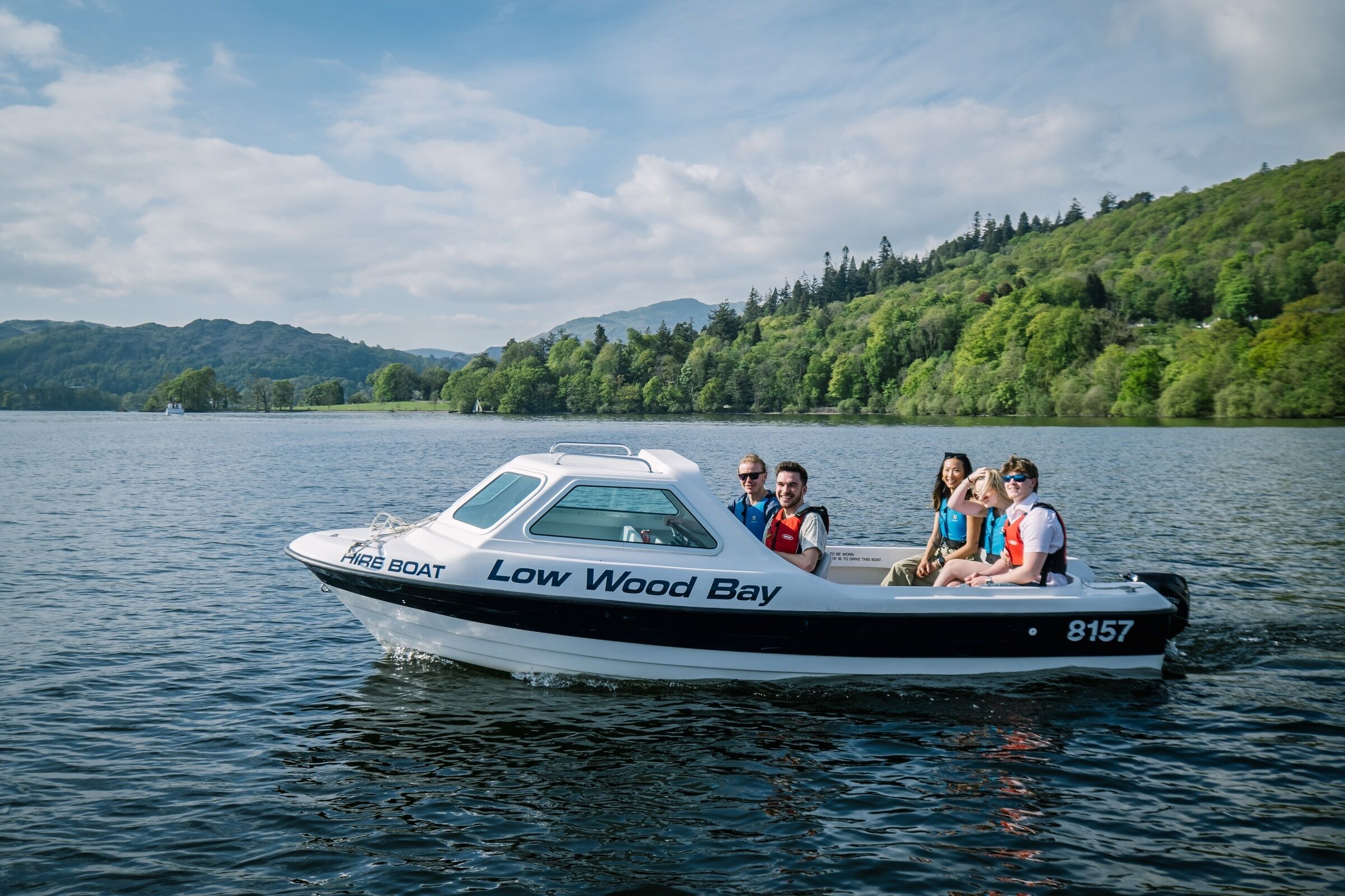 Een boot met 'Low Wood Bay' op de zijkant, die passagiers over een rustig meer vervoert, met heuvels op de achtergrond.