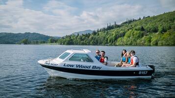 Un barco con la inscripción 'Low Wood Bay' en el costado, transportando pasajeros sobre un lago tranquilo con colinas al fondo.