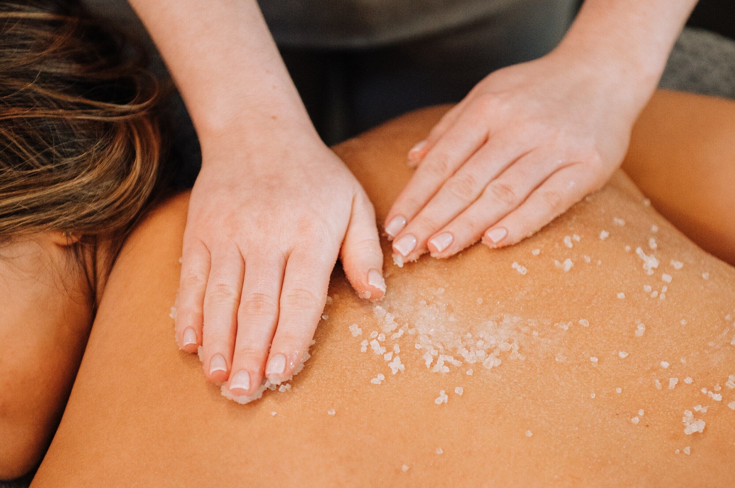 Hands applying salt to a person's back.