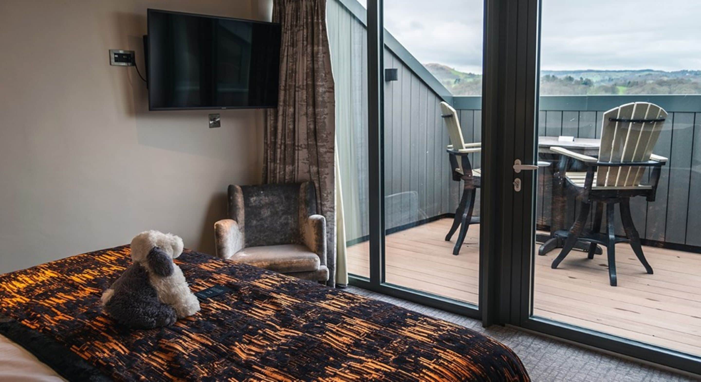 Un dormitorio con cama, una silla, televisión y un balcón con sillas y mesa.