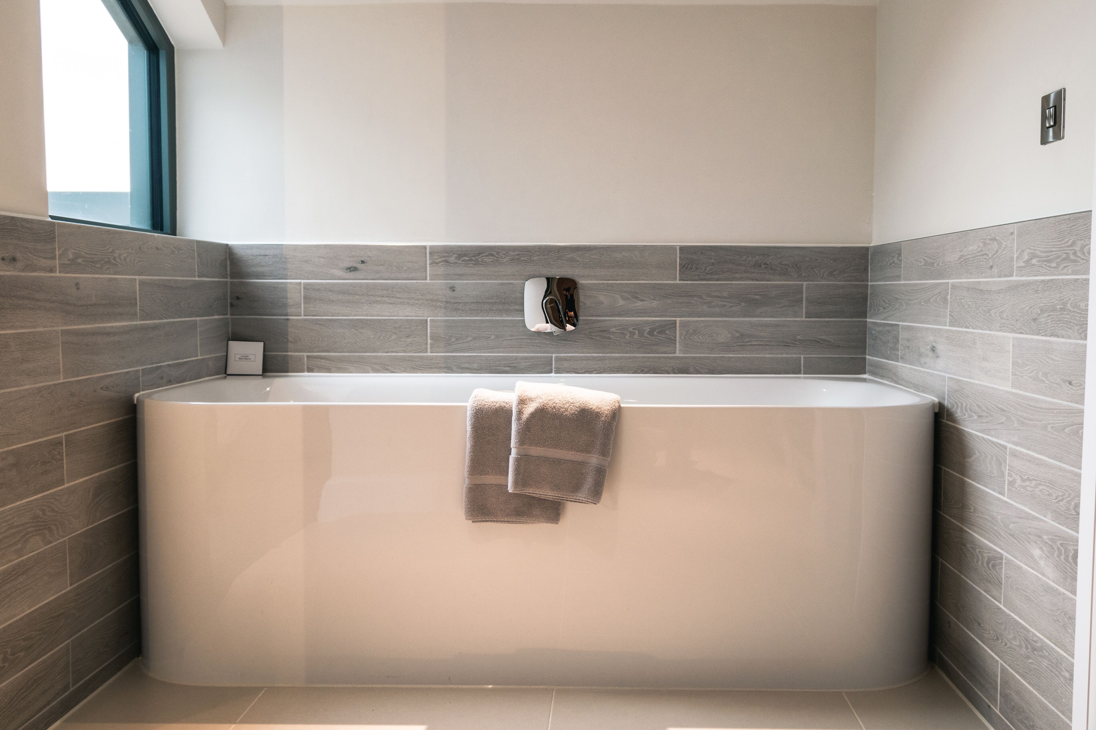 Une salle de bain moderne avec une baignoire sur pieds, des carreaux gris et blancs, et une serviette accrochée au mur.