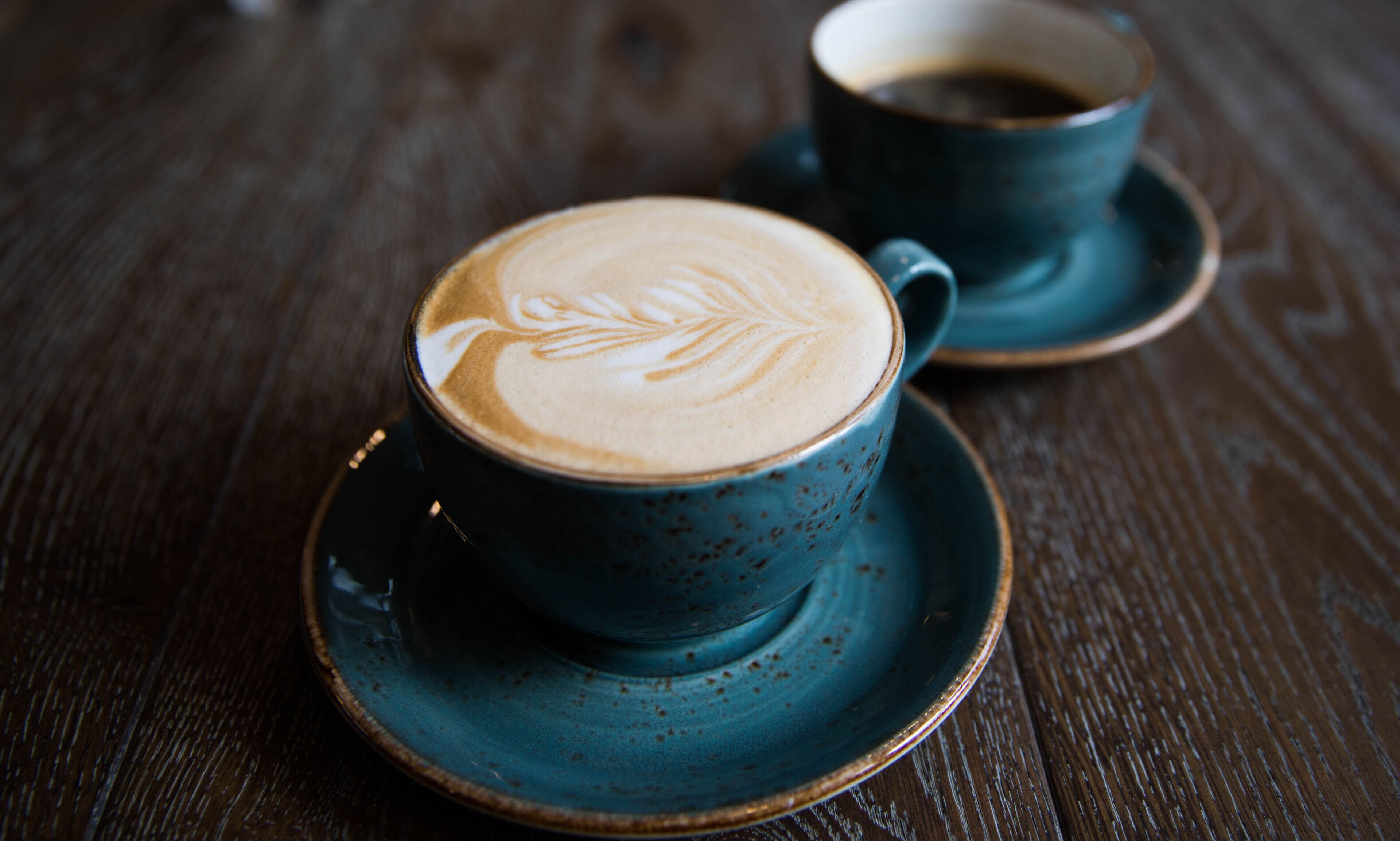 Une tasse de café ornée d’un motif en latte art, posée sur une table en bois.