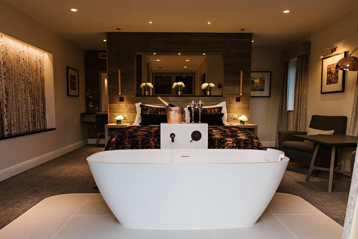 A modern bathroom with a freestanding bathtub, a large mirror, and a seating area with a table and chair.