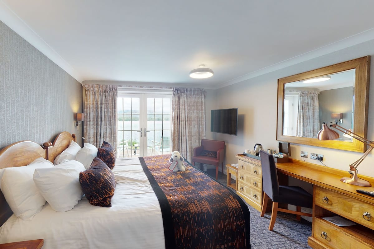 A hotel room with a bed, a desk, a chair, a dresser, a television, and a window with curtains.
