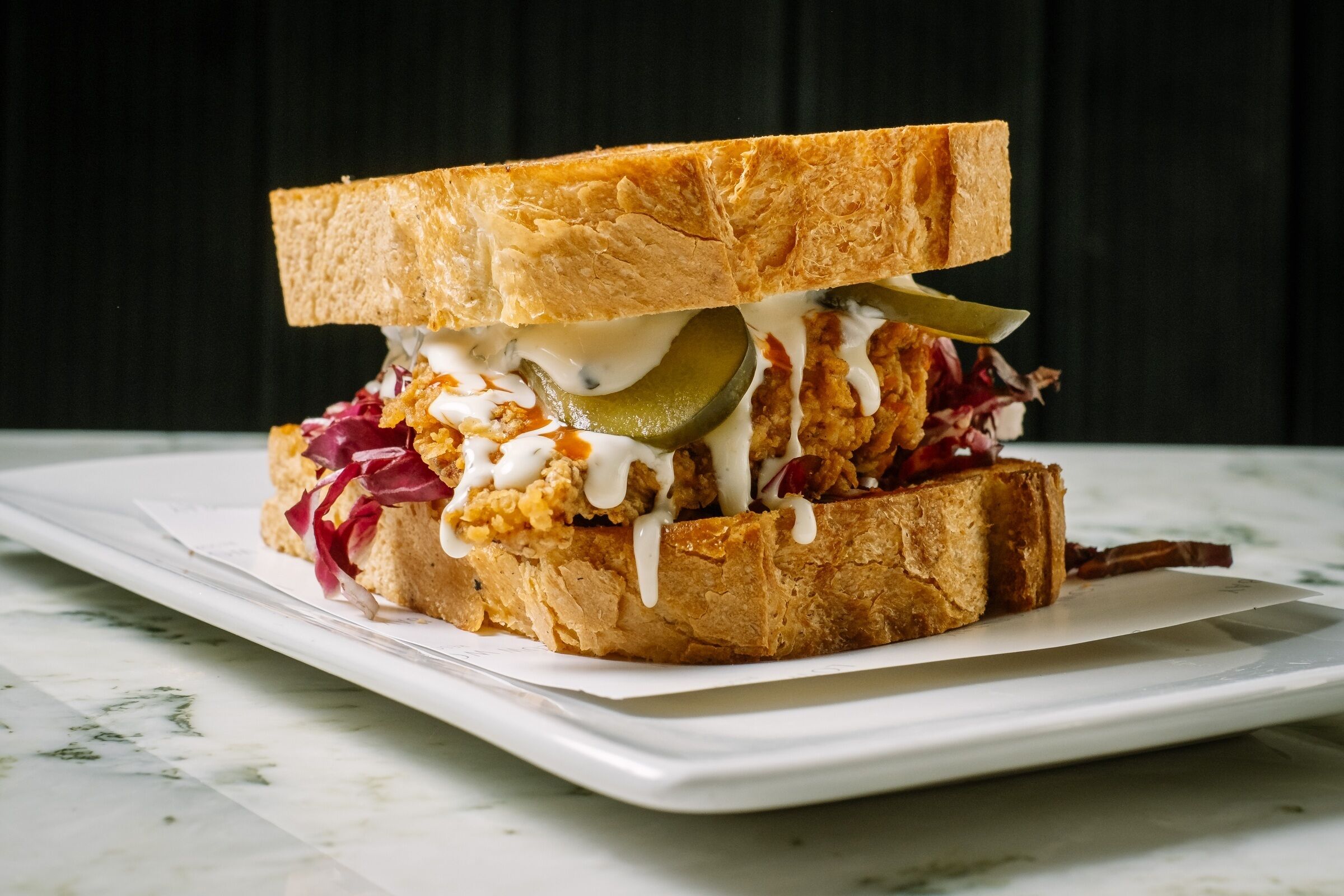 A sandwich with pickles, coleslaw, and a sauce on a white plate.