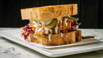 A sandwich with pickles, coleslaw, and a sauce on a white plate.